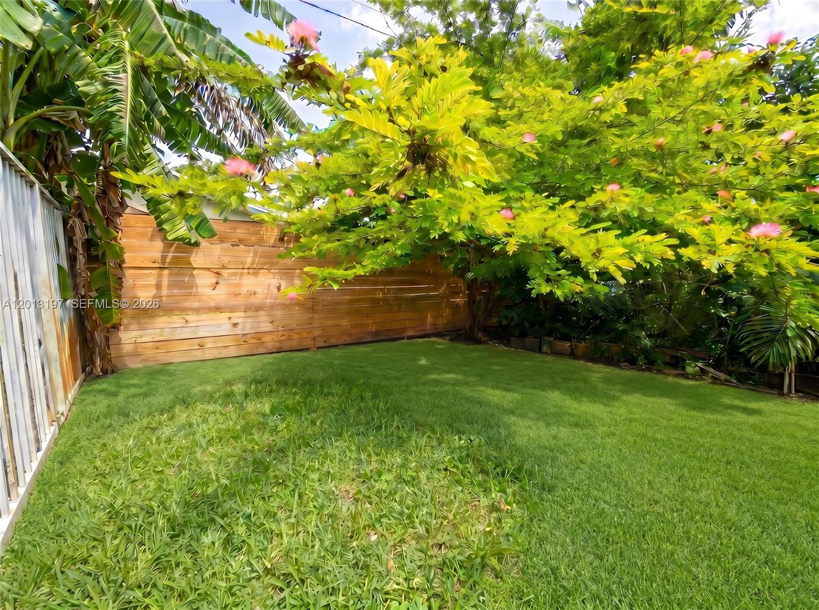 A backyard features a wooden fence, a grassy lawn, and a flowering tree — 21335 NE 19th Ct, Miami FL 33179, MIAMI, FL