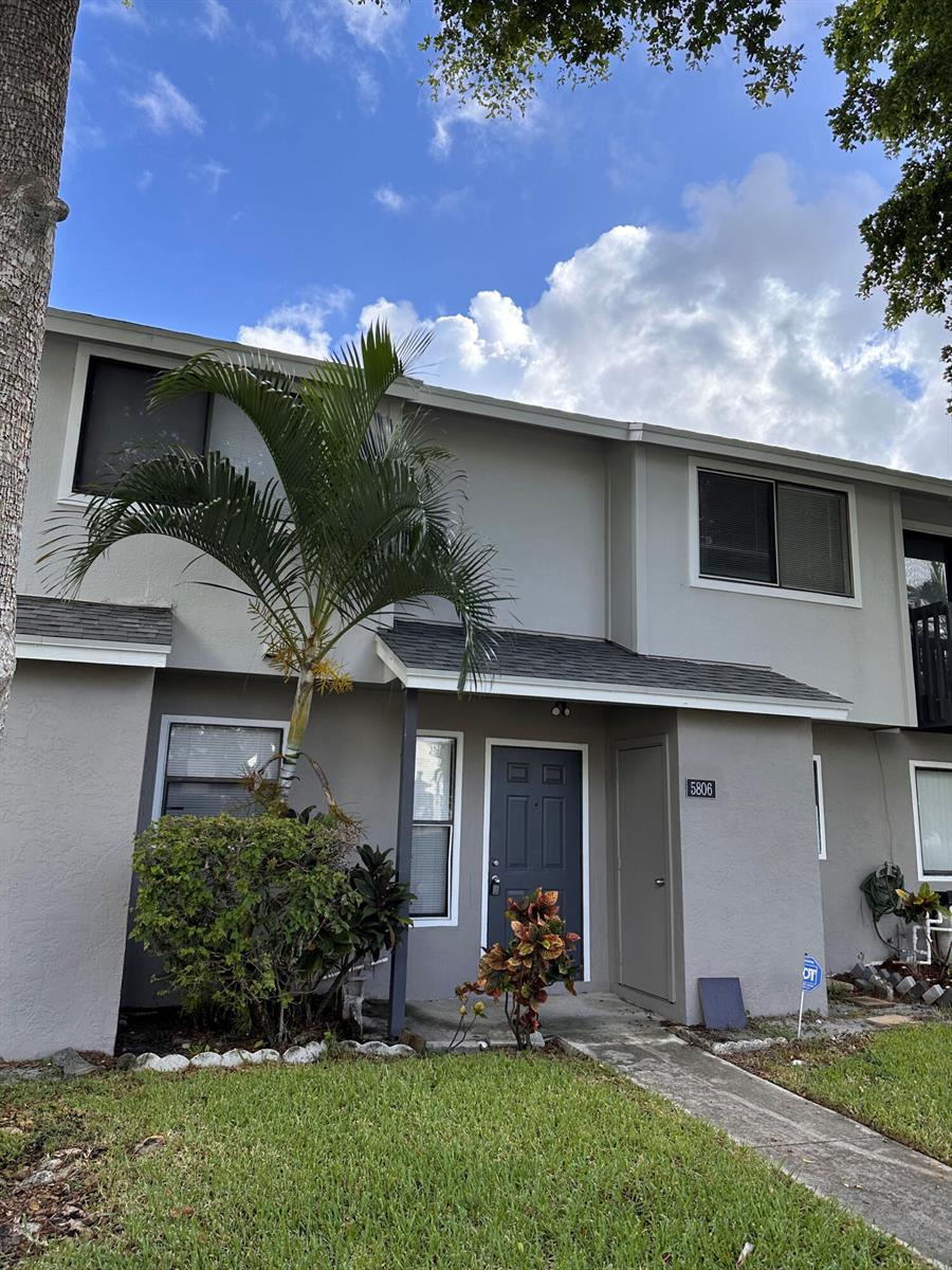 A two-story gray townhouse features a front door, a palm tree, and a small lawn — 5806 Channel Drive, FL 33463, FL