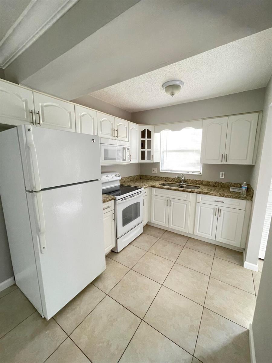 A kitchen features white cabinets, granite countertops, white appliances, and light-colored tile flooring — 5806 Channel Drive, FL 33463, FL