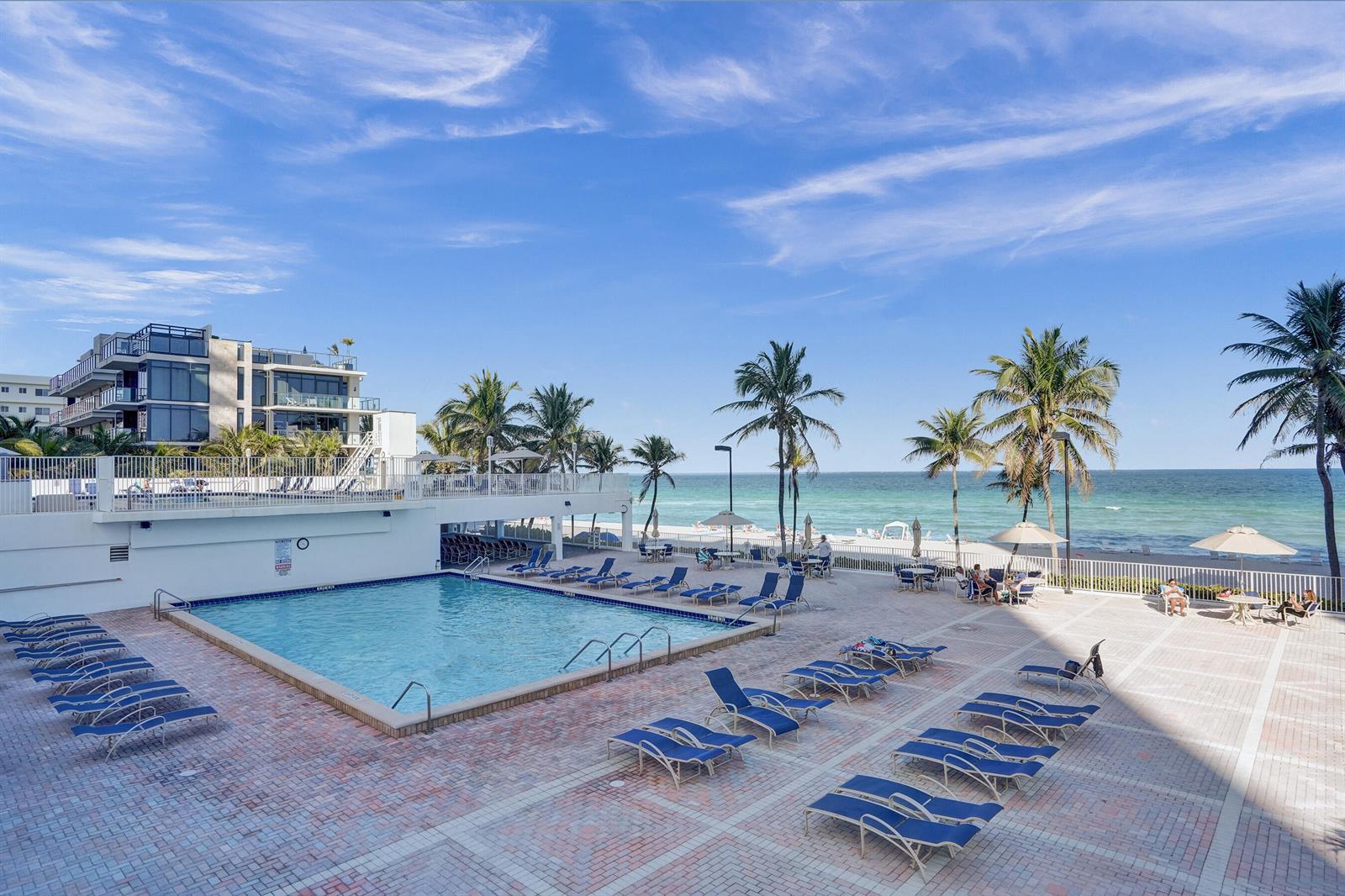 An outdoor swimming pool area with lounge chairs, palm trees, and a view of the ocean — 2301 S Ocean Drive # 1408, Hollywood FL 33019, HOLLYWOOD, FL