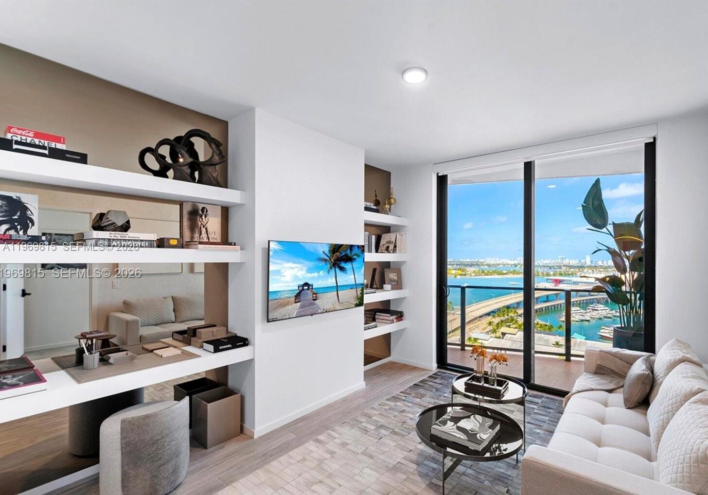 A living room with a desk, built-in shelving, a sofa, and a balcony overlooking water — 398 NE 5th St # 3811, Miami FL 33132, MIAMI, FL