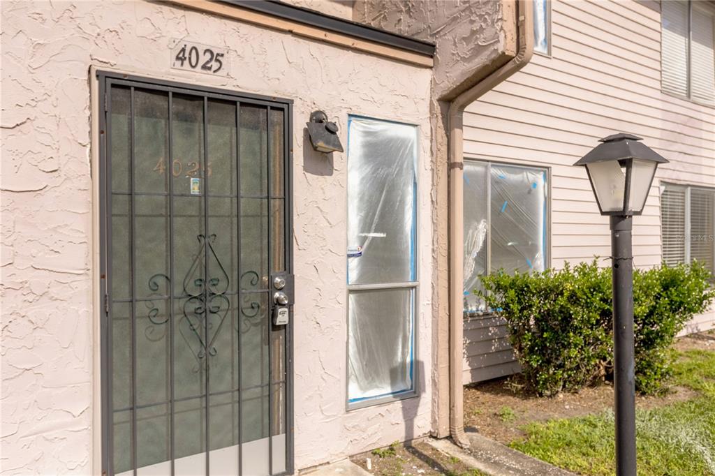 The exterior of a residential unit features a metal security door and windows covered in plastic — 4025 BILLINGSGATE ROAD UNIT 2004, ORLANDO, FL