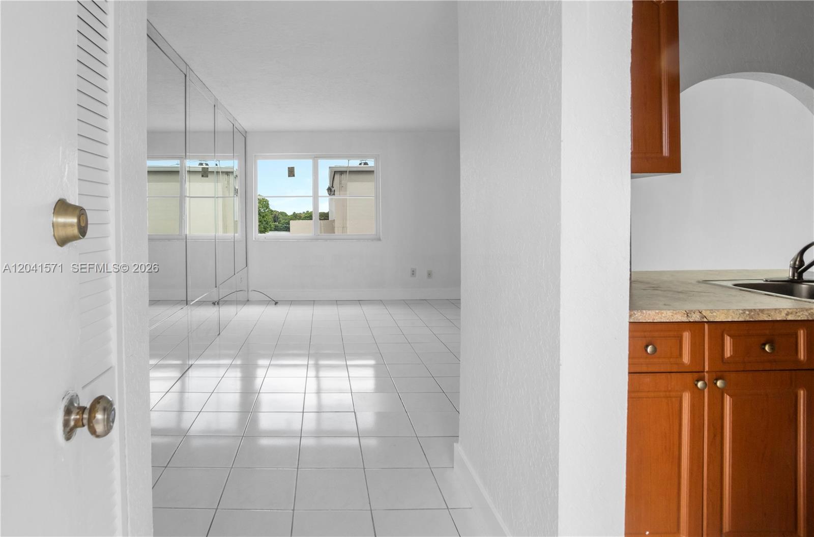 A white-tiled room with mirrored walls is visible through a doorway next to wooden cabinets — 5505 NW 7th St # W404, Miami FL 33126, MIAMI, FL