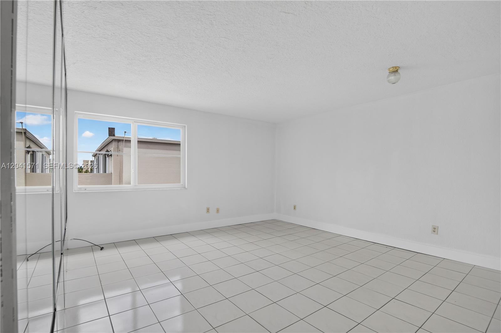 An empty room with white walls, white tile flooring, and a large window — 5505 NW 7th St # W404, Miami FL 33126, MIAMI, FL