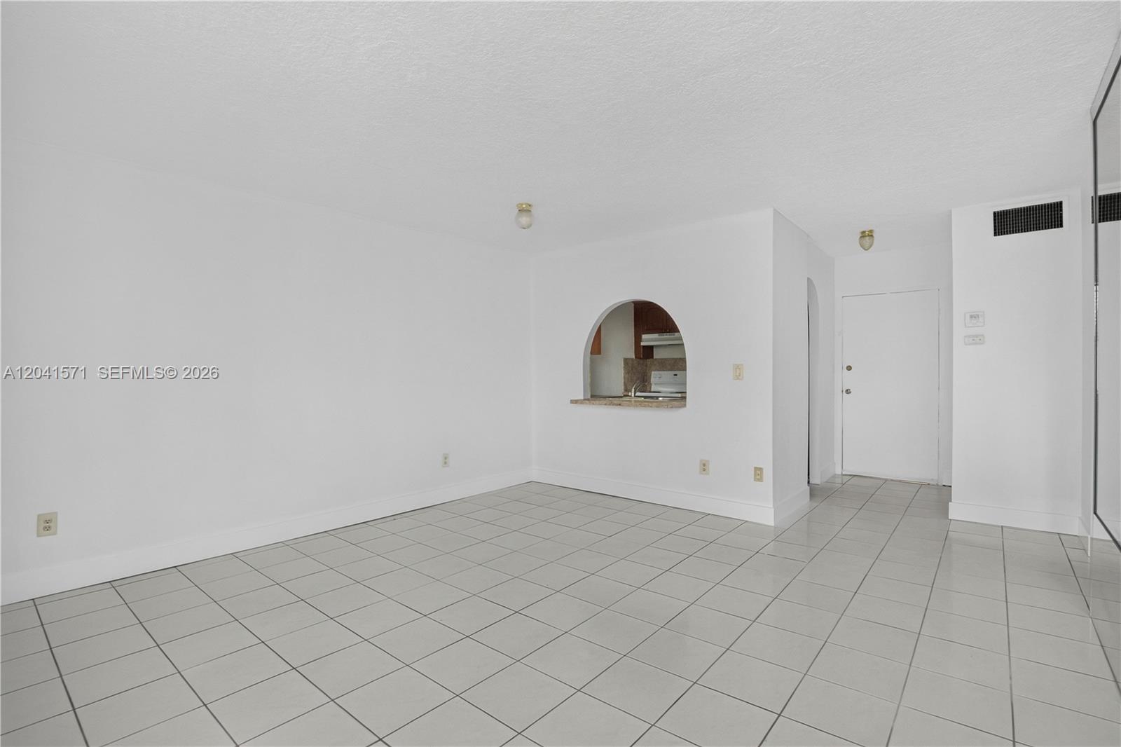 An empty living room features white walls, light-colored floor tiles, and an arched kitchen pass-through — 5505 NW 7th St # W404, Miami FL 33126, MIAMI, FL
