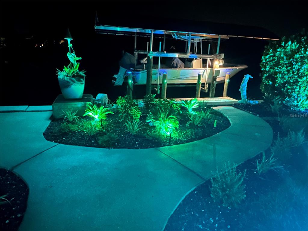 A boat on a lift sits behind a landscaped garden illuminated by green landscape lights — 4255 SPIRE STREET, PORT CHARLOTTE, FL