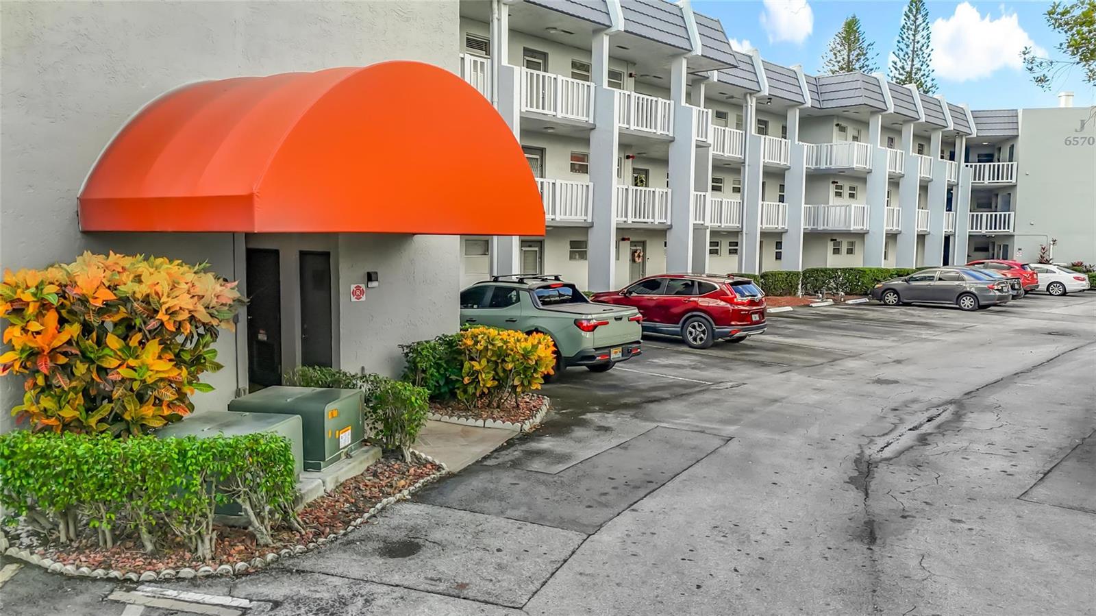 An exterior view of a multi-story apartment building with a prominent orange entrance awning — 6570 Royal Palm Boulevard # 312, Margate FL 33063, MARGATE, FL