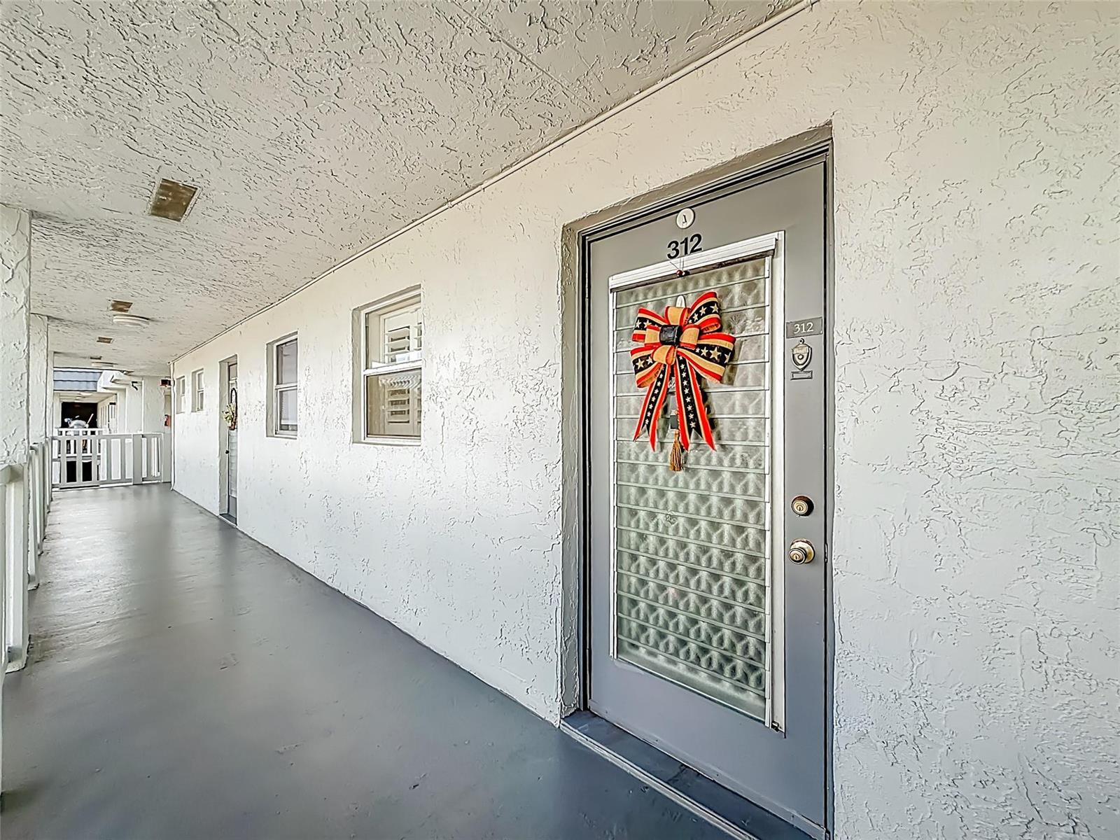 An exterior walkway leads to a grey door marked 312 with a decorative bow — 6570 Royal Palm Boulevard # 312, Margate FL 33063, MARGATE, FL