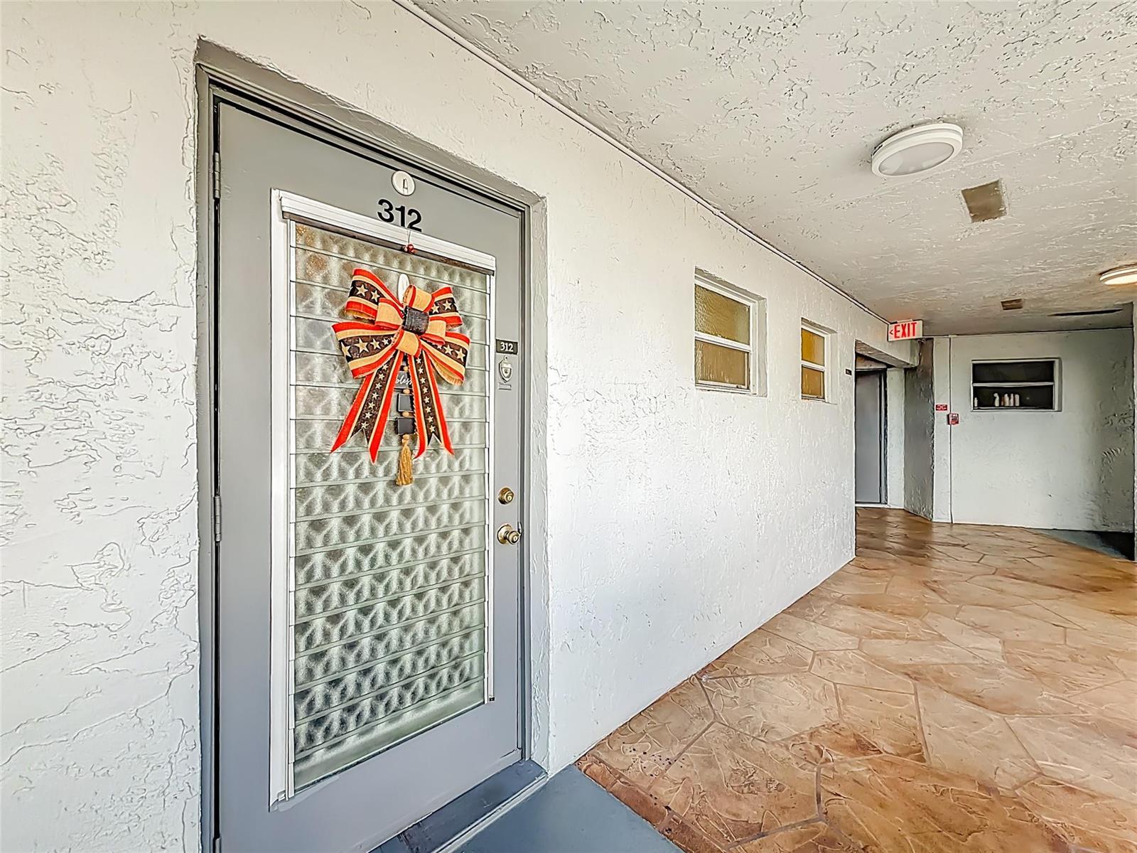 A gray apartment door with a decorative bow sits in a textured white hallway — 6570 Royal Palm Boulevard # 312, Margate FL 33063, MARGATE, FL