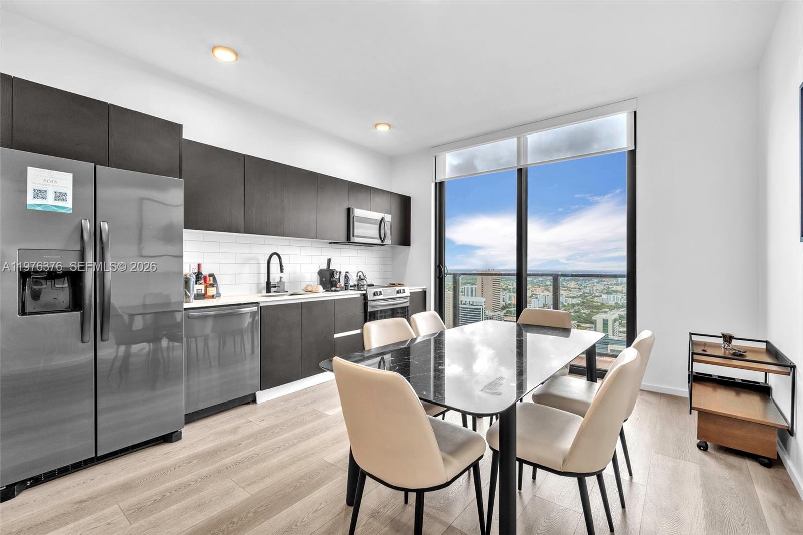 A modern kitchen and dining area features dark cabinetry, stainless appliances, and floor-to-ceiling windows — 398 NE 5th St # 4701, Miami FL 33132, MIAMI, FL