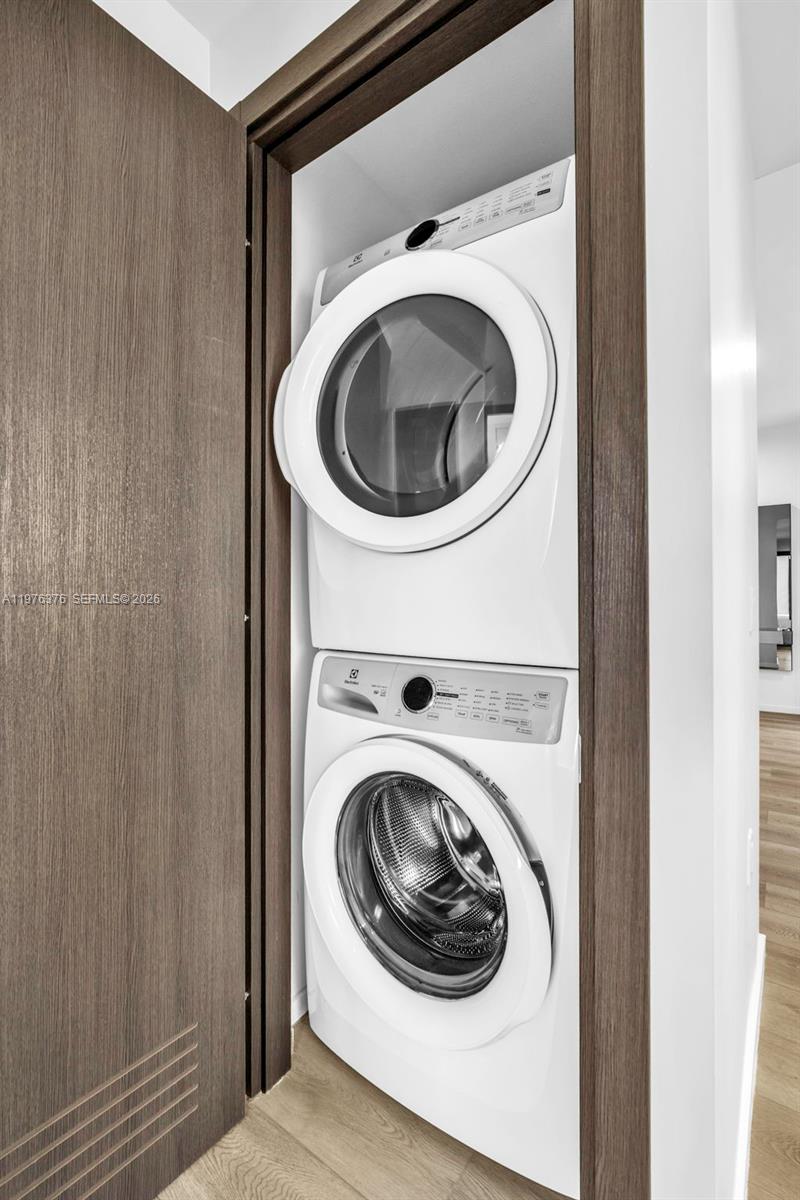 A stacked white washer and dryer unit is installed inside a closet with wood-toned doors — 398 NE 5th St # 4701, Miami FL 33132, MIAMI, FL