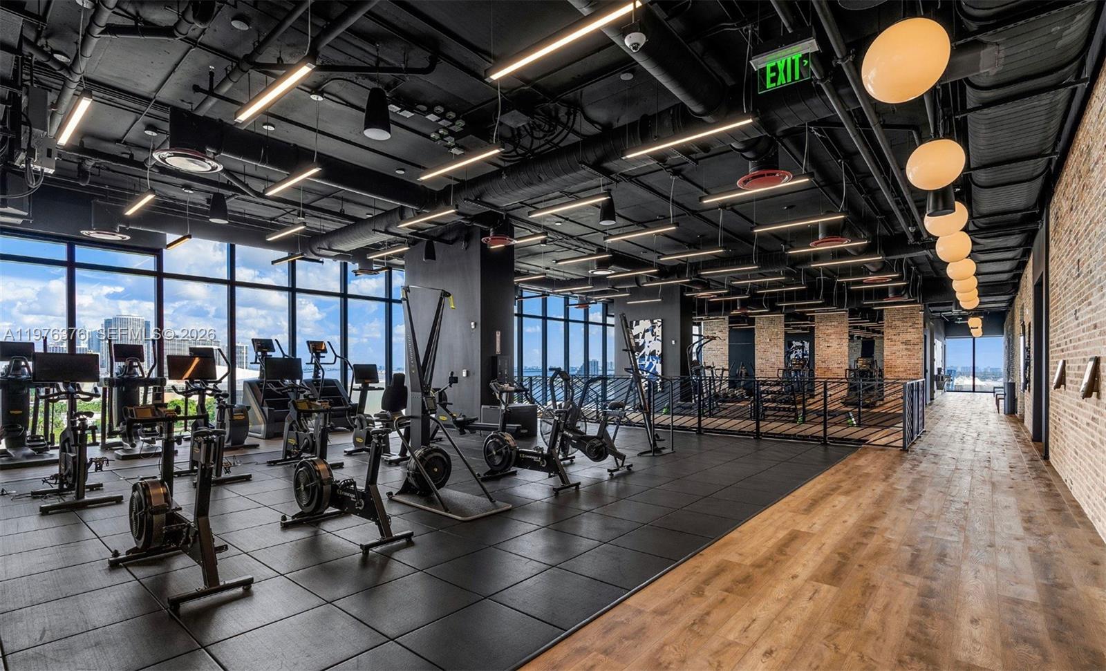 A modern gym features black rubber flooring, exposed industrial ceilings, and floor-to-ceiling windows with views — 398 NE 5th St # 4701, Miami FL 33132, MIAMI, FL