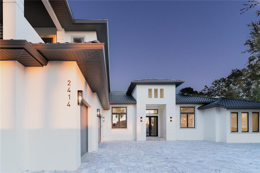 A modern white house exterior with a paved driveway, dark roof, and vertical house numbers — 2414 BAYSHORE ROAD, NOKOMIS, FL