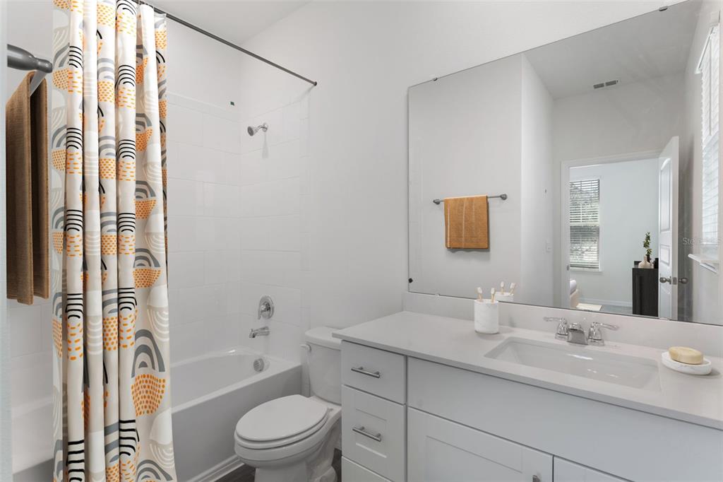 A bathroom features a white vanity, a toilet, and a shower-tub combo with a patterned curtain — 11864 SHINE VIEW LANE, WINTER GARDEN, FL