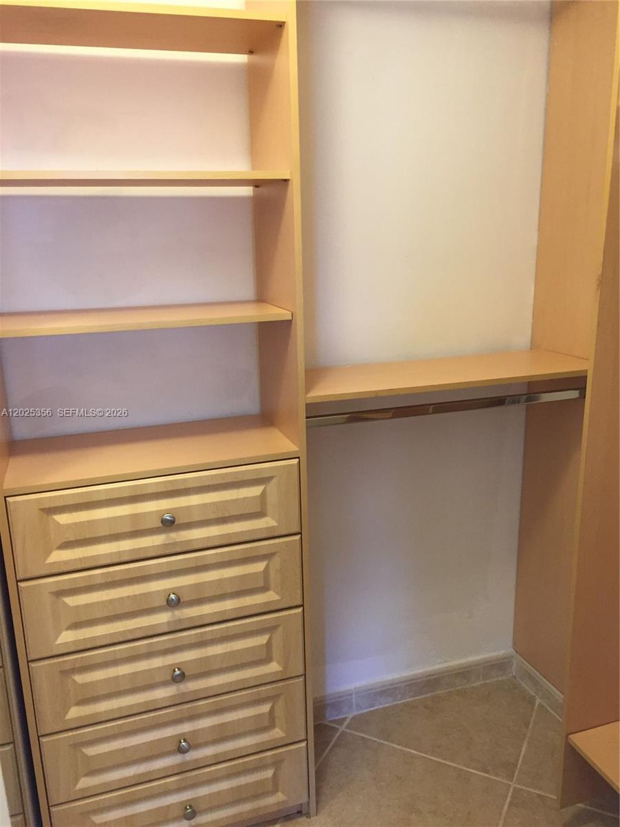 A white stacked washer and dryer unit sits in a closet with built-in shelving — 15570 SW 76th Ln # 9, Miami FL 33193, MIAMI, FL