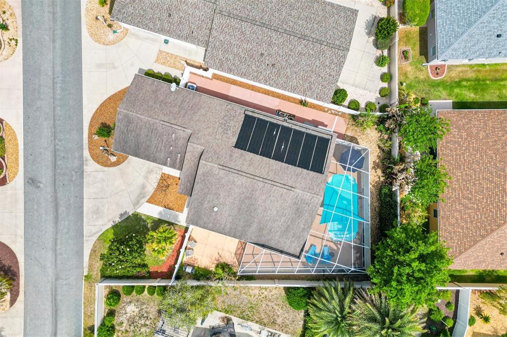 An aerial view shows a house with a solar-paneled roof and a screened-in pool — 1936 NEEDLEWOOD LANE, THE VILLAGES, FL