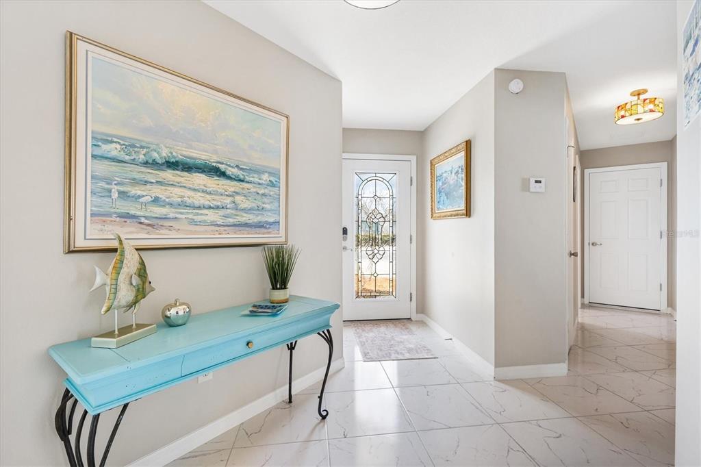 A bright entryway features light-colored tile floors, a turquoise console table, and a glass-paneled door — 1936 NEEDLEWOOD LANE, THE VILLAGES, FL
