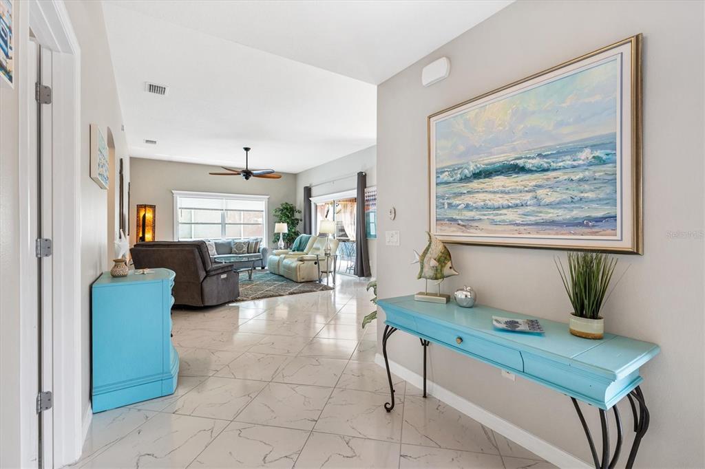 A bright entryway with tiled floors leads into a living room with a ceiling fan — 1936 NEEDLEWOOD LANE, THE VILLAGES, FL