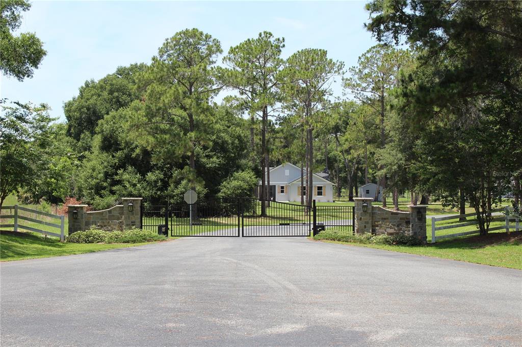 A gated entrance with stone pillars leads to a house surrounded by trees and grass — 3117 BRIGHT LAKE CIRCLE lot 63, GROVELAND, FL