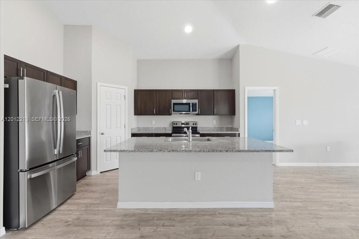A modern kitchen features dark wood cabinets, granite countertops, stainless steel appliances, and wood-look flooring — 1536 Axel Circle, Winter Haven FL 33880, WINTER HAVEN, FL