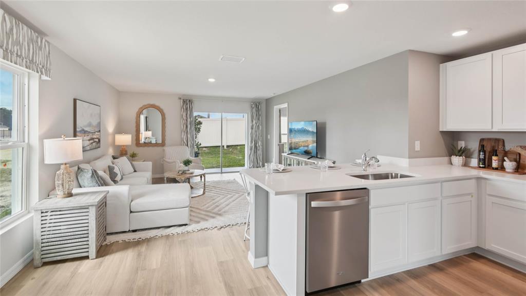 An open-concept kitchen with white cabinets overlooks a living room with a sliding glass door — 3070 EVENMORE WAY, WILDWOOD, FL