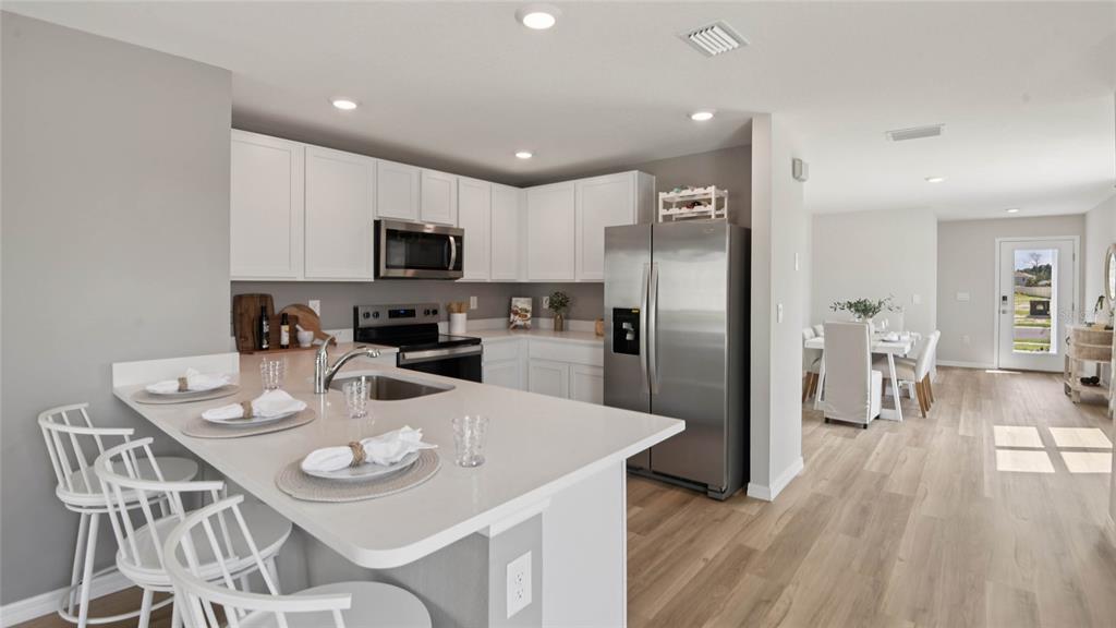 A kitchen features white cabinets, stainless steel appliances, a quartz island, and light wood flooring — 3070 EVENMORE WAY, WILDWOOD, FL