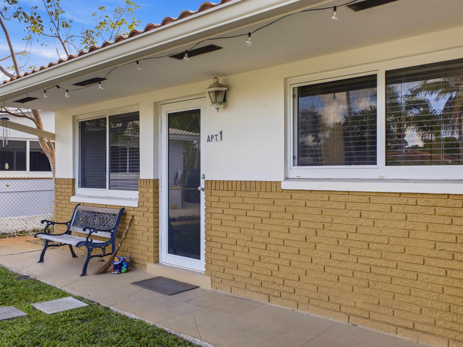 An exterior view of an apartment entrance with a brick facade and a metal bench — 451 SE 1st Avenue # B, Pompano Beach FL 33060, POMPANO BEACH, FL