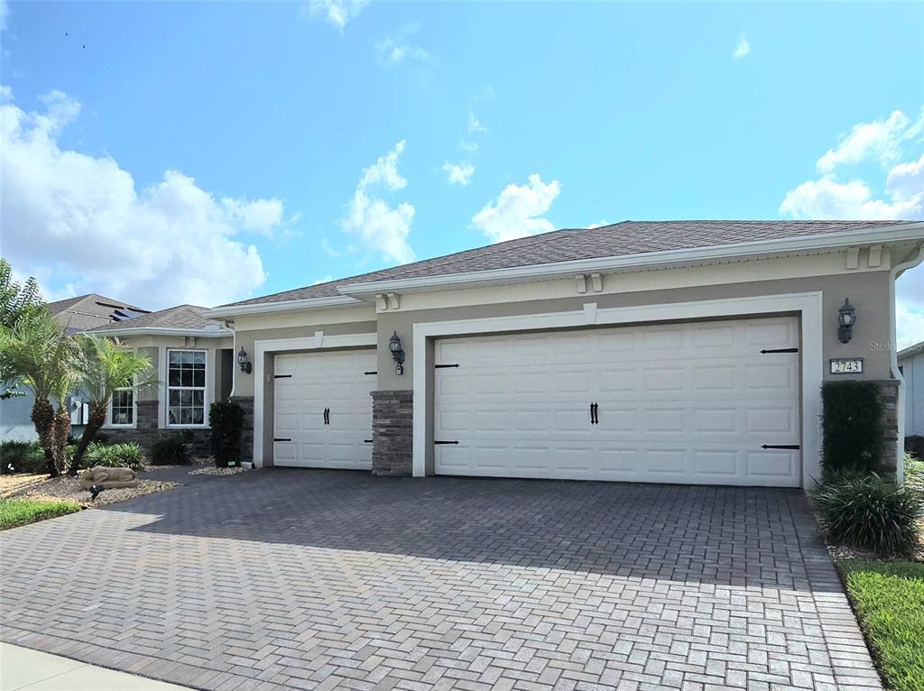 A beige house with a three-car garage and a paved driveway under a blue sky — 2743 RIVER CREEK LANE, ST CLOUD, FL