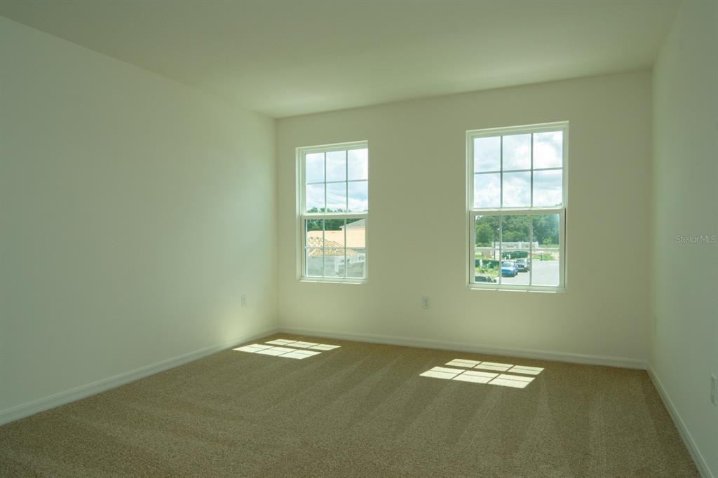 An empty bedroom with beige carpet, white walls, and two windows overlooking a construction site — 1673 SWAN SWIM DRIVE, DAVENPORT, FL
