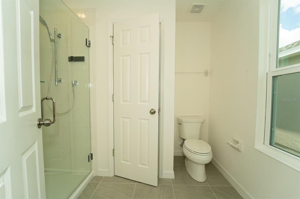 A bathroom features a glass-enclosed shower, a white toilet, and light gray tile flooring — 1673 SWAN SWIM DRIVE, DAVENPORT, FL