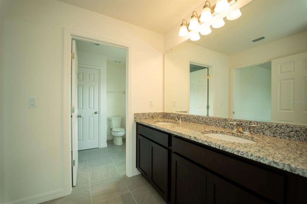 A bathroom features a double-sink granite vanity with dark cabinets and a large wall mirror — 1673 SWAN SWIM DRIVE, DAVENPORT, FL