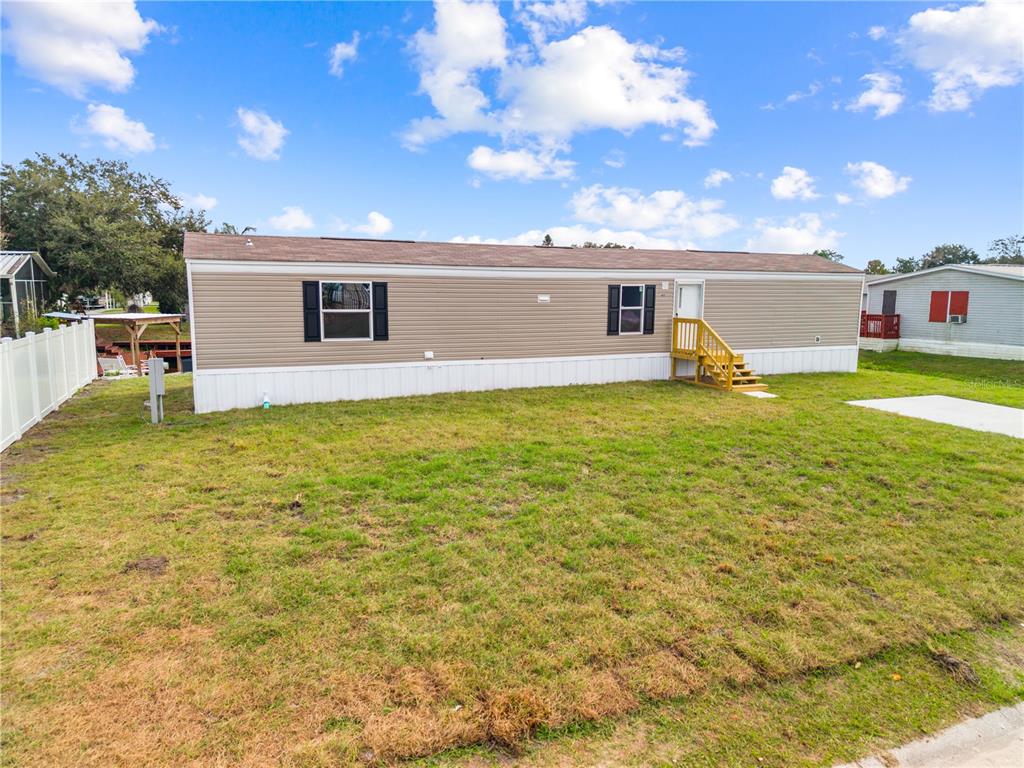A tan mobile home with a brown roof and wooden stairs sits on a lawn — 411 LAGOON COURT, KENANSVILLE, FL