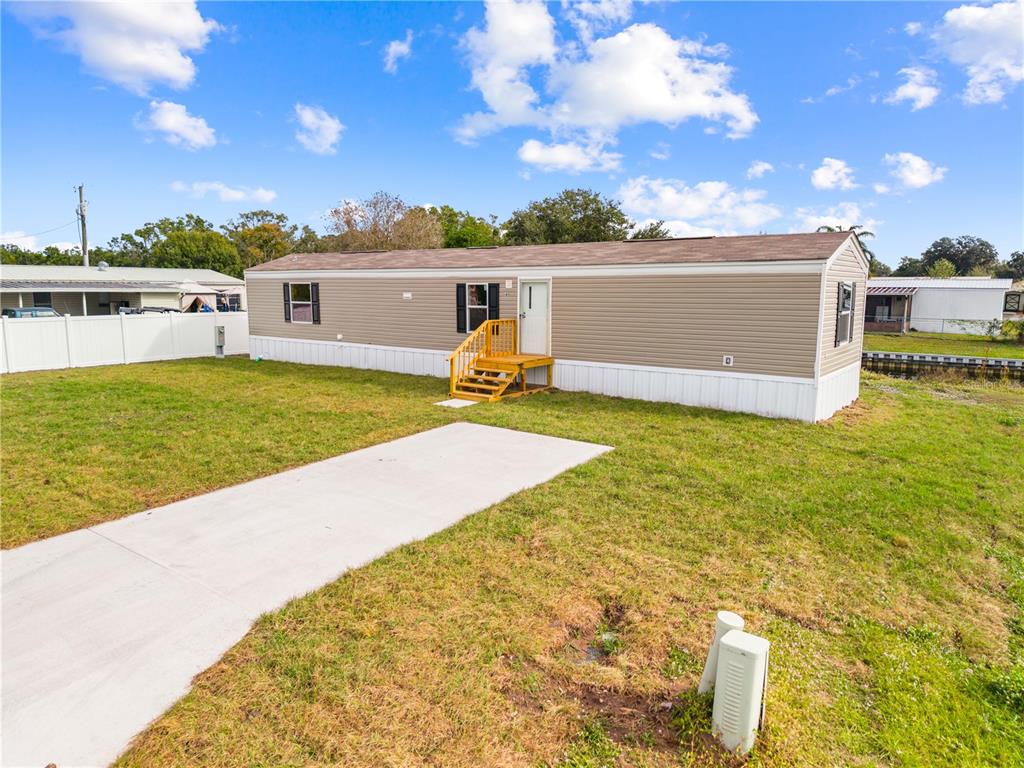 A tan mobile home with a brown roof sits on a grassy lot with a driveway — 411 LAGOON COURT, KENANSVILLE, FL