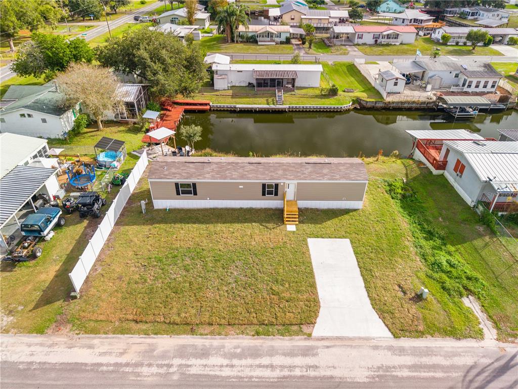 An aerial view shows a tan mobile home with a concrete driveway and canal access — 411 LAGOON COURT, KENANSVILLE, FL