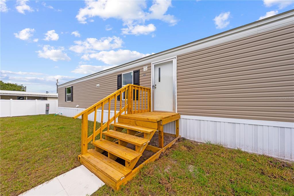 A tan mobile home exterior features a wooden staircase leading to a white entry door — 411 LAGOON COURT, KENANSVILLE, FL