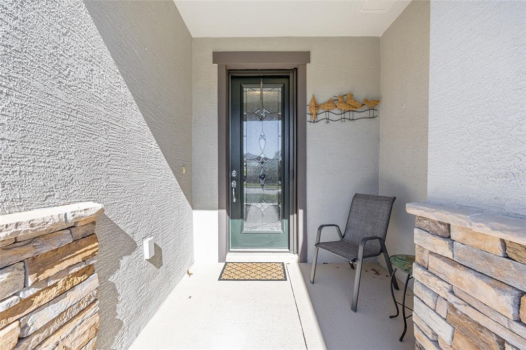 A covered entryway features a dark green front door, a gray chair, and stone accents — 9601 SW 65TH PLACE, OCALA, FL