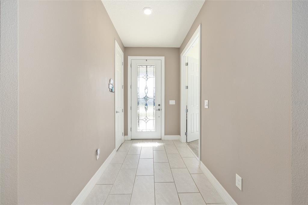 A brightly lit entryway features light-colored tile flooring, beige walls, and a decorative glass door — 9601 SW 65TH PLACE, OCALA, FL