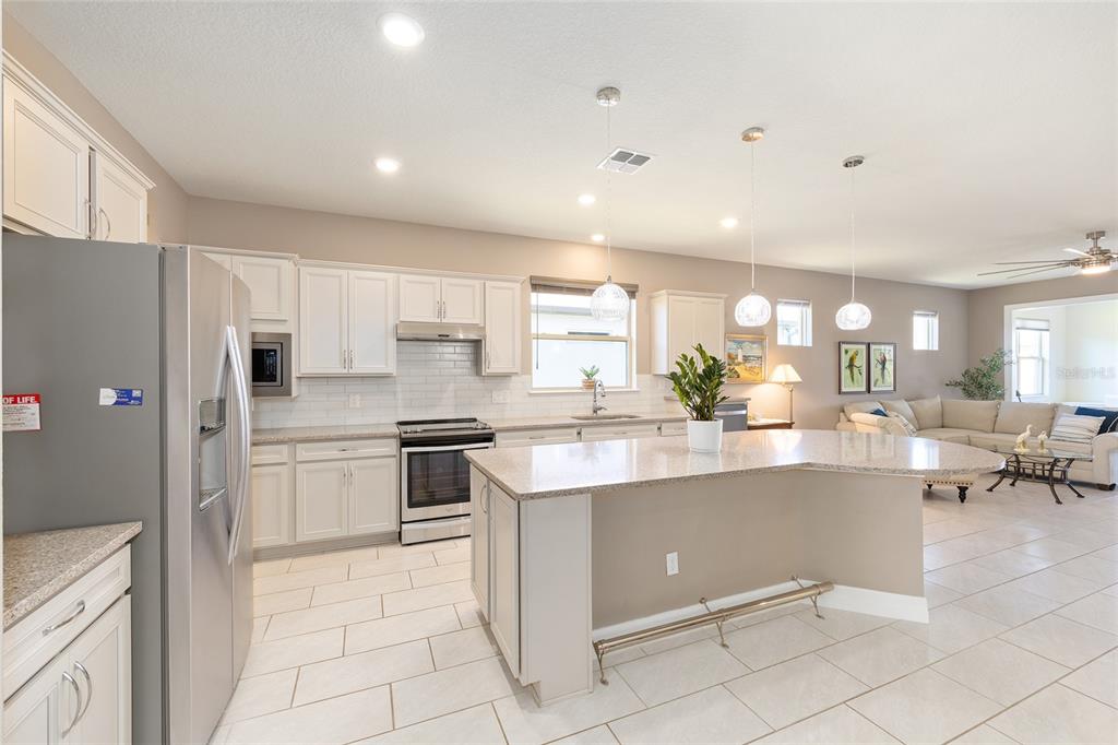 A modern kitchen with white cabinets, granite countertops, and an island opens to a living area — 9601 SW 65TH PLACE, OCALA, FL