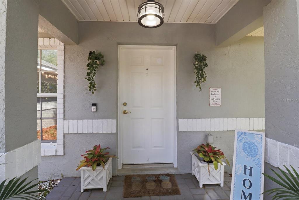 A covered front porch features a white door, two potted plants, and a welcome mat — 8667 N UPLAND DRIVE, CITRUS SPRINGS, FL