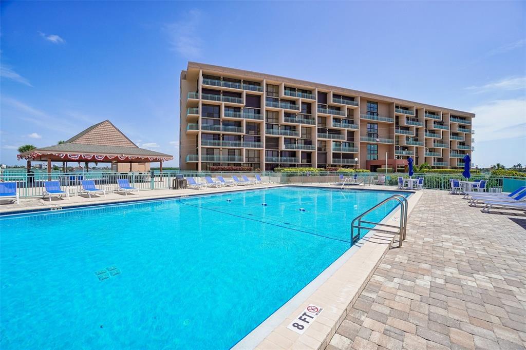 A large swimming pool sits in front of a multi-story apartment building with balconies — 1 KEY CAPRI UNIT 406W, ST PETERSBURG, FL