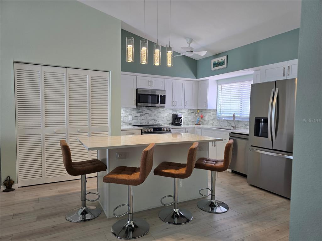A kitchen features a white island with four brown barstools, stainless steel appliances, and teal walls — 6468 HAMLET DRIVE UNIT 4B, ENGLEWOOD, FL