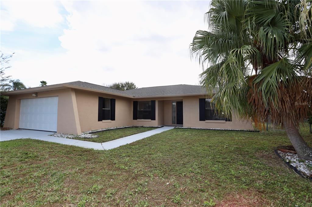 A single-story tan house with a white garage door and a palm tree in front — 620 HERALDO COURT, KISSIMMEE, FL