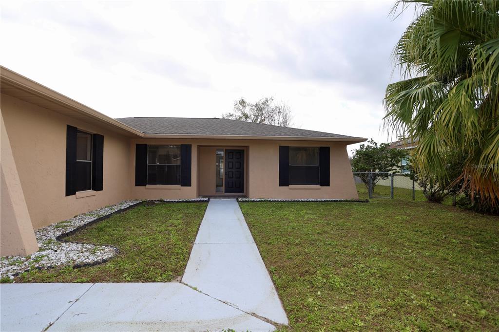 A single-story tan house with black shutters and a concrete walkway leading to the entrance — 620 HERALDO COURT, KISSIMMEE, FL