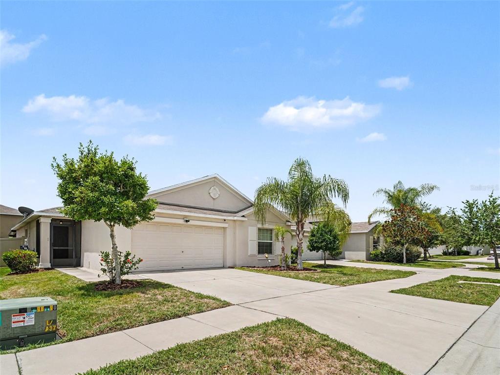 A single-story suburban house features a two-car garage, a concrete driveway, and palm trees — 16803 PEACEFUL VALLEY DRIVE, WIMAUMA, FL