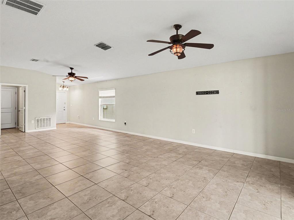 A large, empty room features light-colored tile flooring, two ceiling fans, and neutral walls — 16803 PEACEFUL VALLEY DRIVE, WIMAUMA, FL