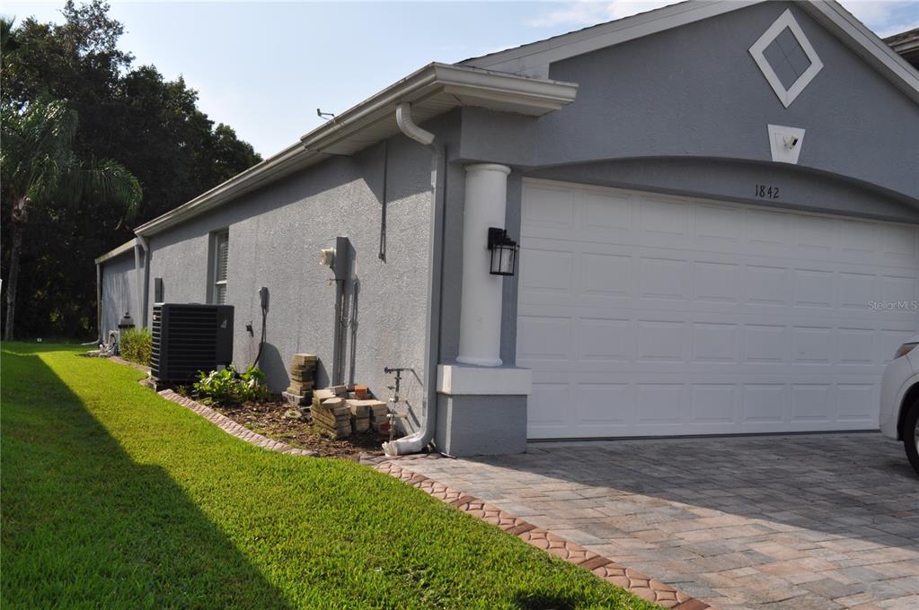 The exterior of a gray house features a two-car garage, a paver driveway, and landscaping — 1842 RIDGELAKE COURT, WESLEY CHAPEL, FL
