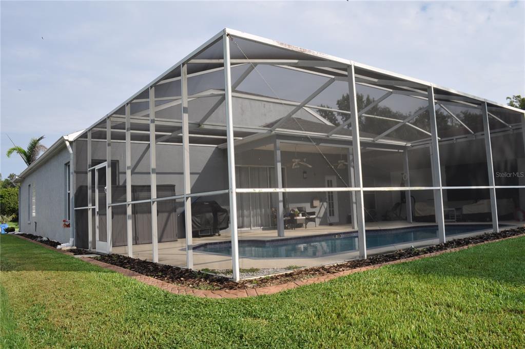 A swimming pool enclosed by a screened lanai sits behind a house with gray siding — 1842 RIDGELAKE COURT, WESLEY CHAPEL, FL