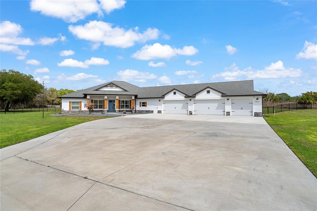 A single-story house with a large concrete driveway and a three-car garage — 4821 SUNNYSIDE DRIVE, FRUITLAND PARK, FL