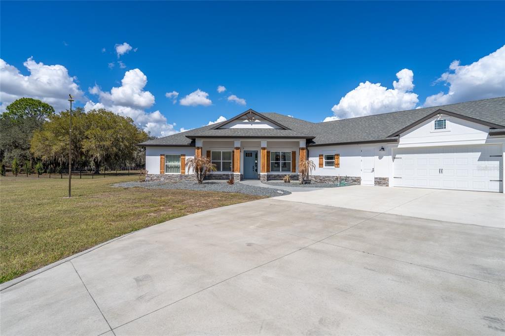 A single-story house with a white exterior, stone accents, and a concrete driveway — 4821 SUNNYSIDE DRIVE, FRUITLAND PARK, FL