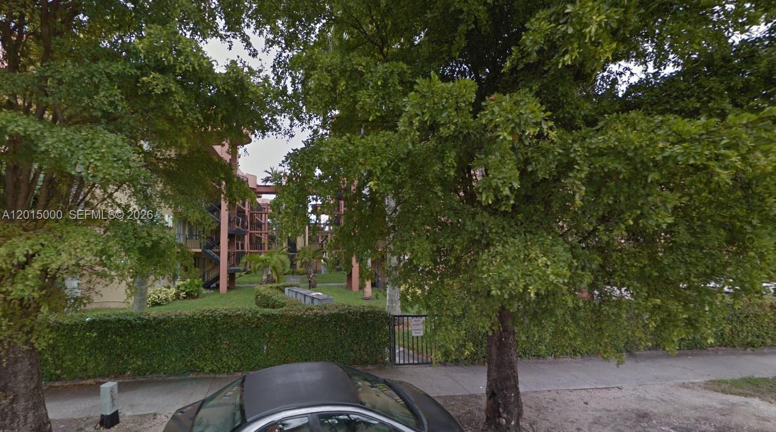 An exterior view of a multi-story apartment building partially obscured by large trees — 5490 W 21st Ct # 313, Hialeah FL 33016, HIALEAH, FL